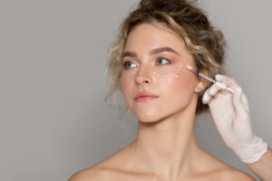 Headshot of a young, beautiful woman getting dermal filler injected under her eyes to prevent future skin issues